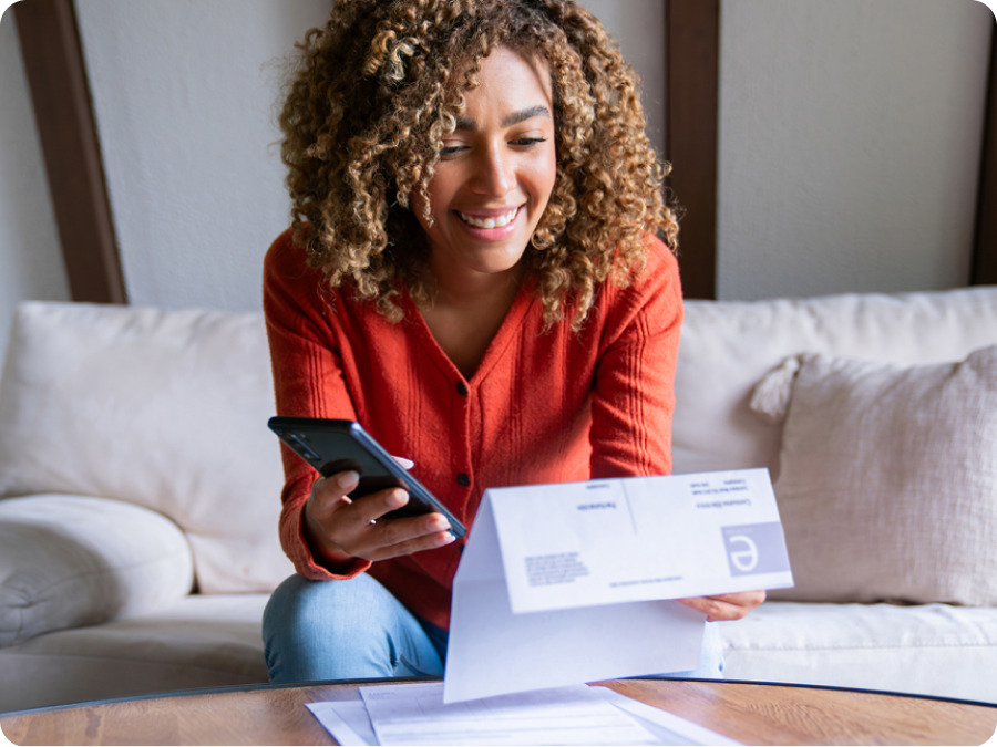 Smiling woman holding a utility bill and her phone on the couch, splitting the bill payment in two with Zip Pay in 2