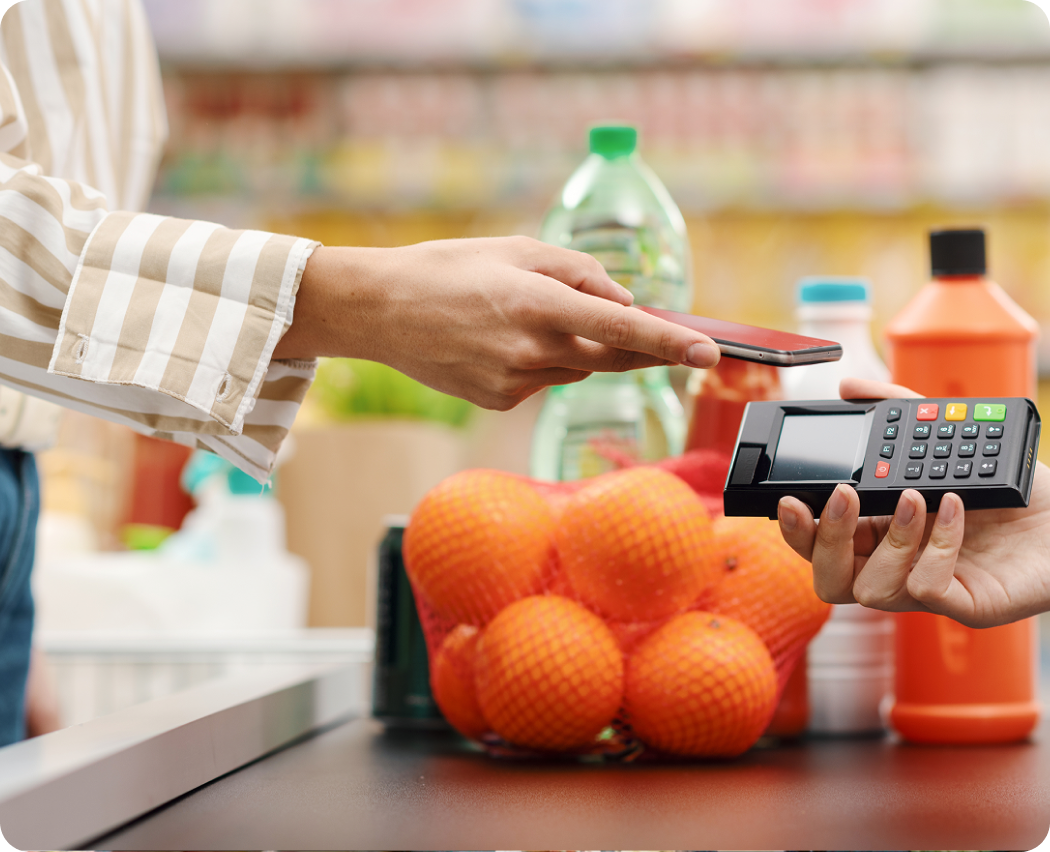Shopper tapping a phone on a card reader at a grocery checkout counter to pay for oranges with Zip buy now, pay later