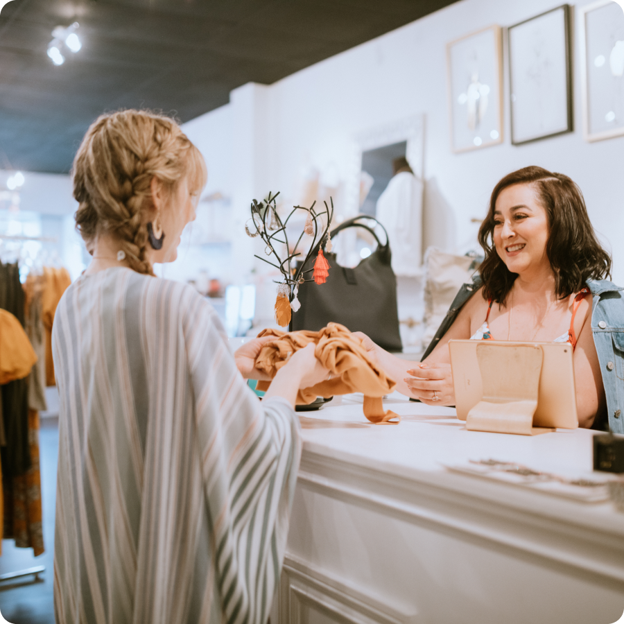 Smiling cashier handing a shopper her purchase at the counter of a clothing boutique that offers Zip buy now, pay later