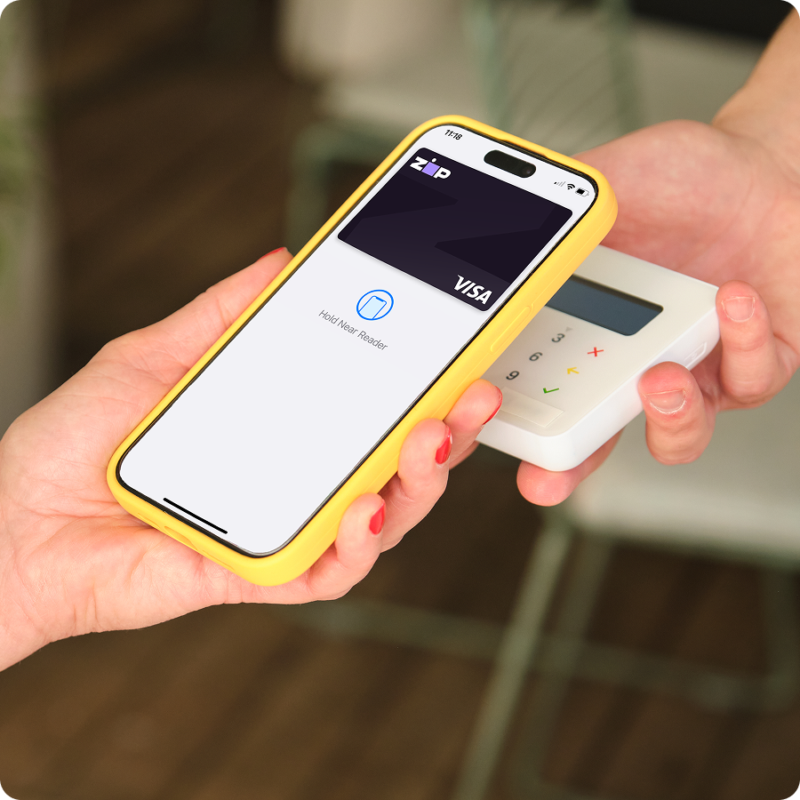 Shopper paying in store with Zip buy now, pay later by tapping a phone with a Zip Visa card on a contactless card reader.
