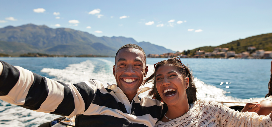 Couple laughing on a boat trip with mountains behind them, illustrating travel booked with Zip buy now, pay later