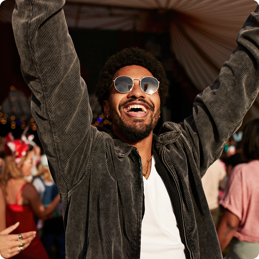 Excited man in sunglasses cheering with arms raised in a crowd at a live event, buying tickets with Zip buy now, pay later