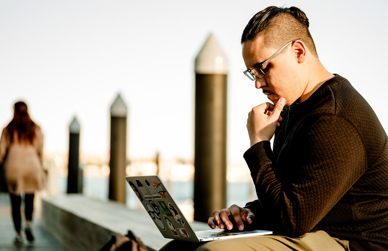 Photo of Nick DeJesus working on his laptop while sitting near the waterfront.