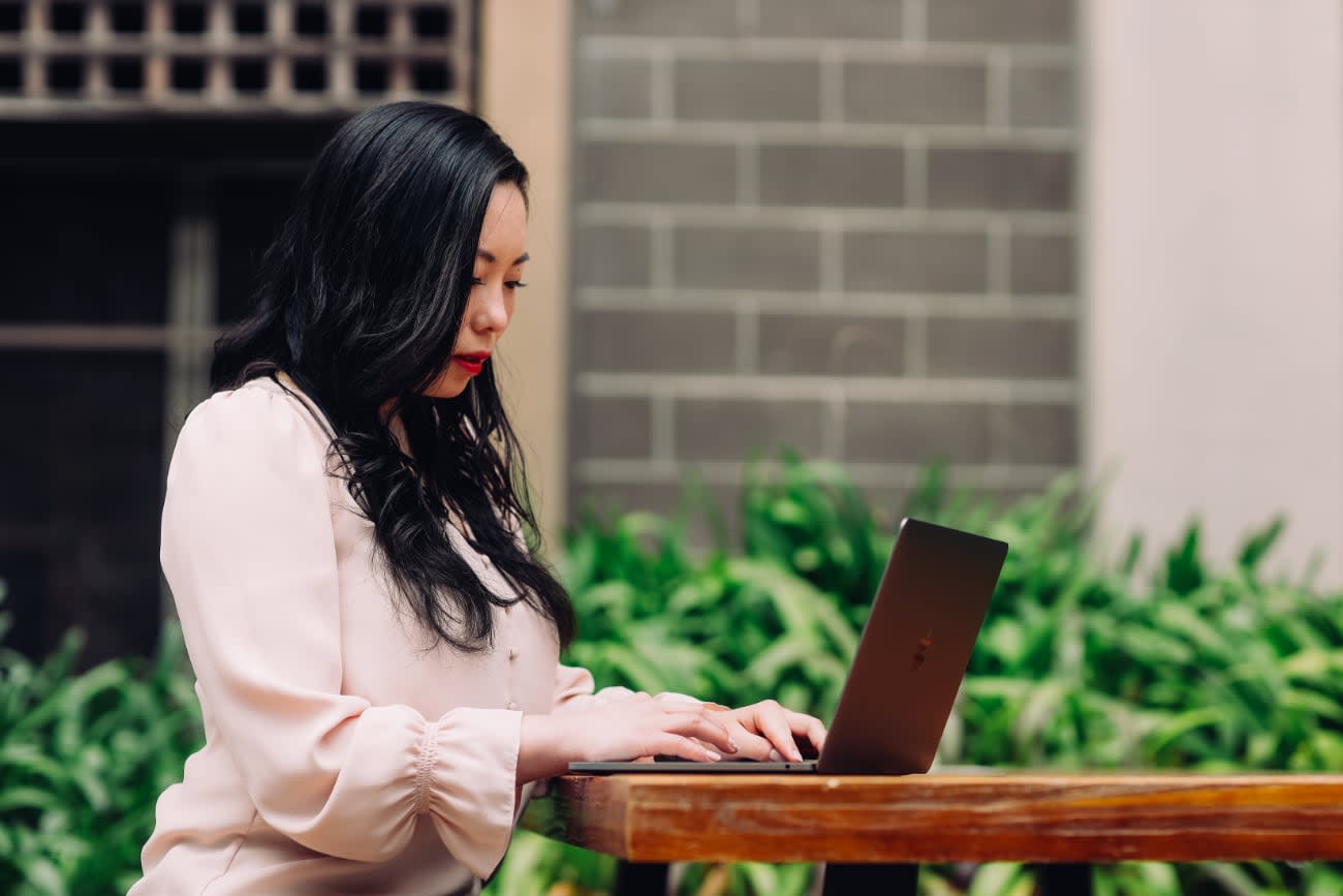 Photo of Shirley Wu outdoors, working on her laptop.