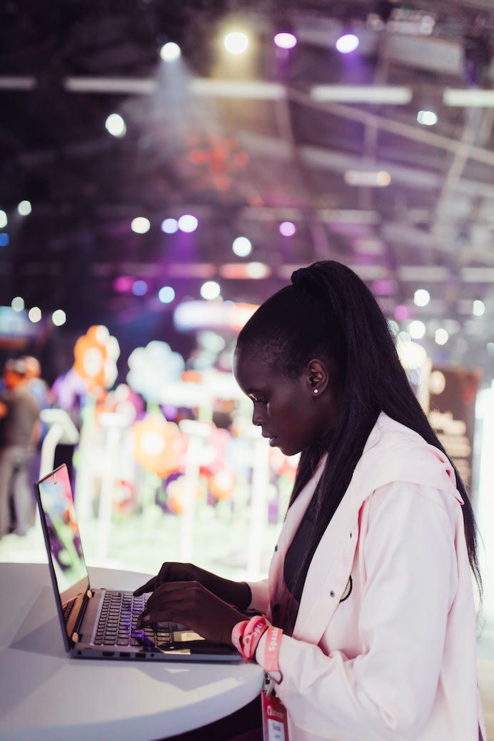 Photo of Sonia John working on a laptop with a GitHub Universe 'Speaker' badge around their wrist.