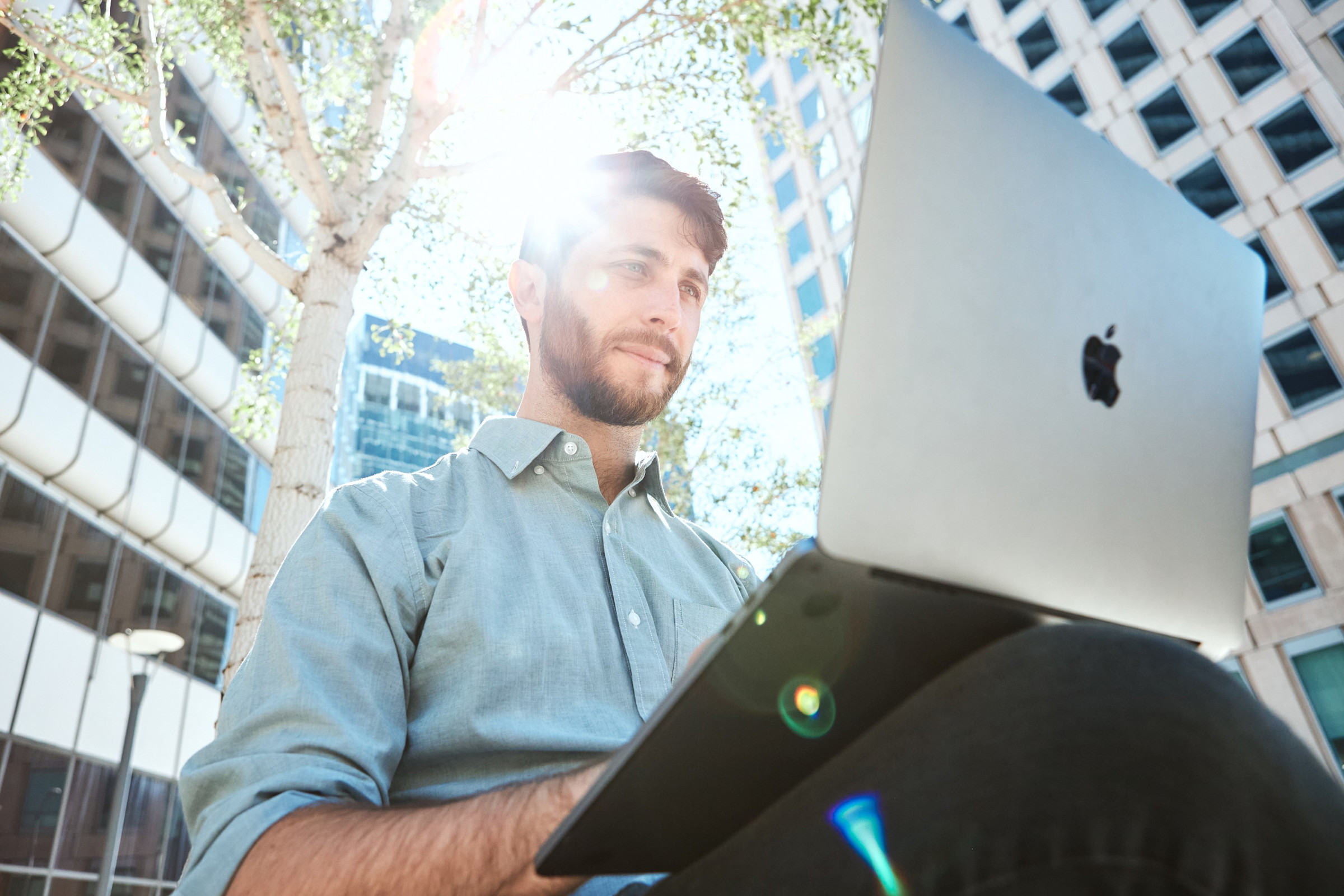 Author Avi working on his laptop with an urban landscape and the sun behind him