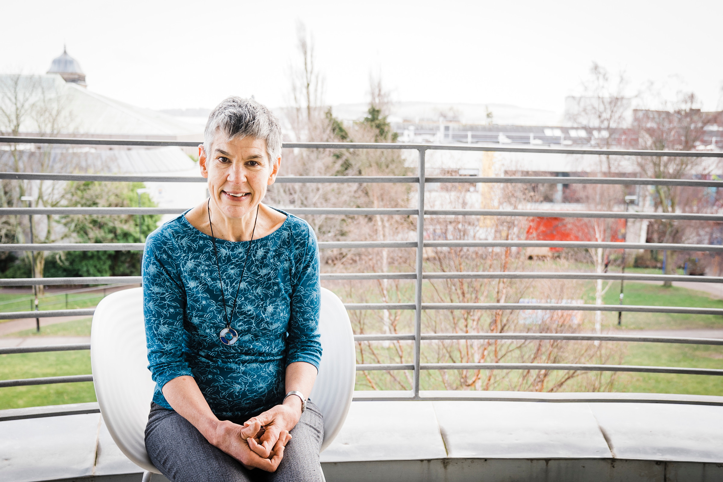 In a blue shirt, Annalu sits outside on a balcony on the University of Dundee campus.