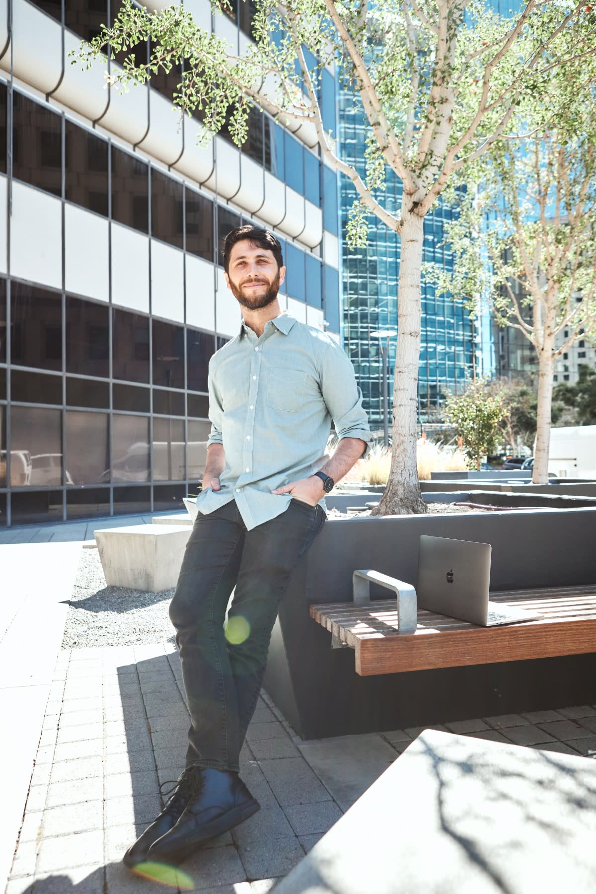 Author Avi standing outside with his computer next to an urban landscape