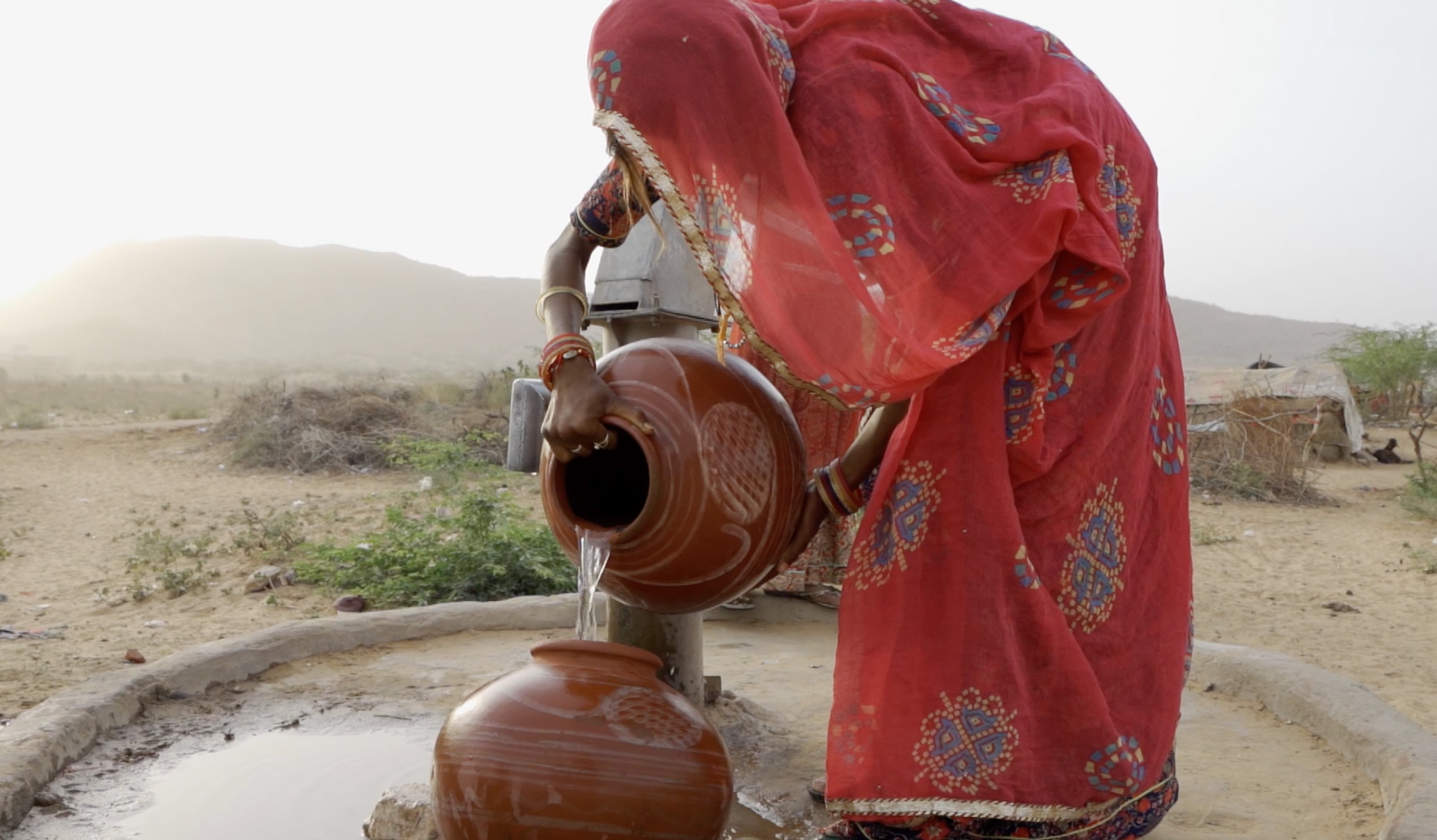 A woman in a sari pouring water from one clay pot into the other