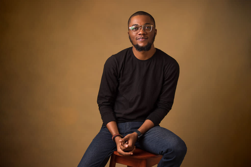 Author Adewale smiling and sitting on a stool