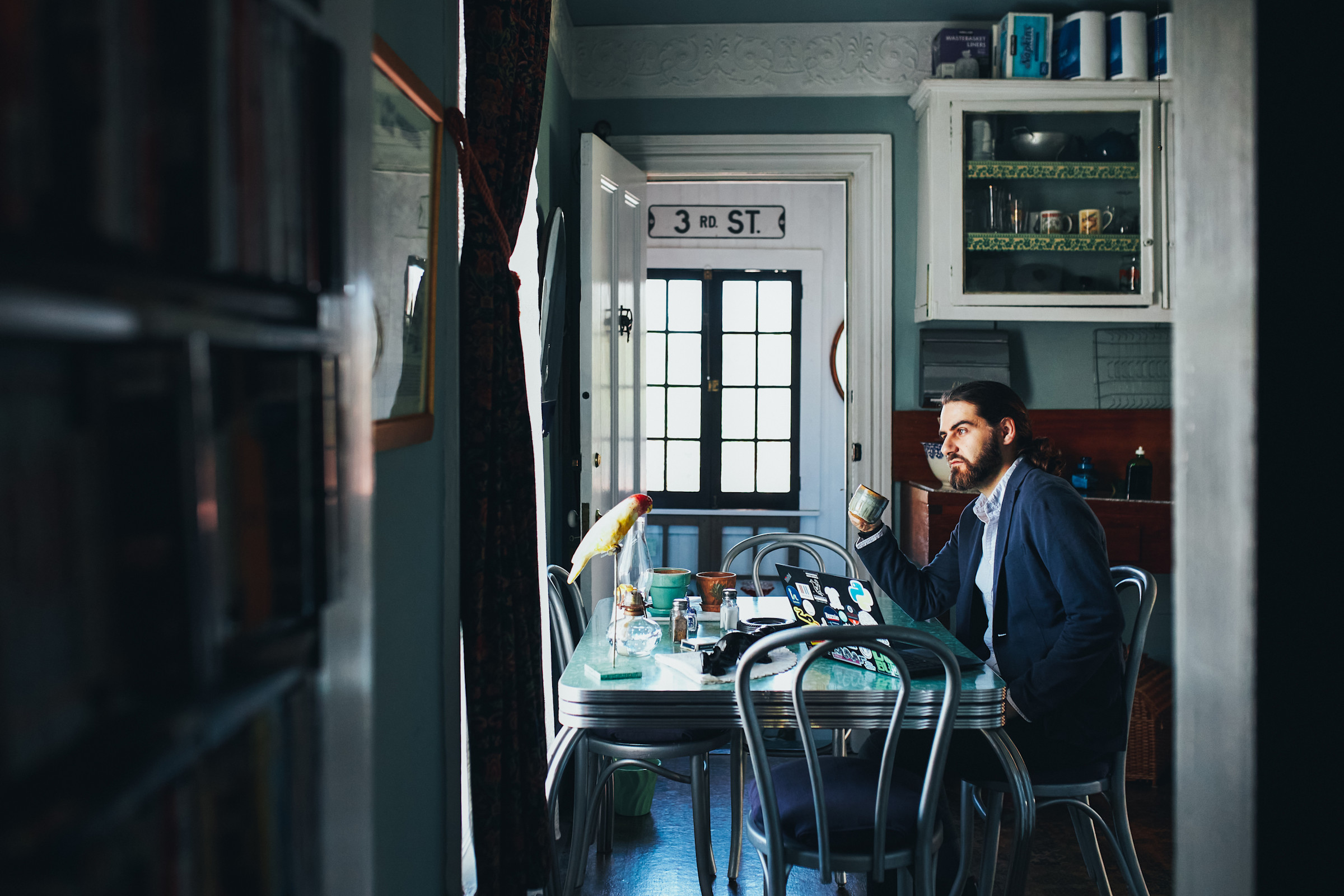 Author Mahmoud sitting with his laptop in his kitchen across from a pet bird