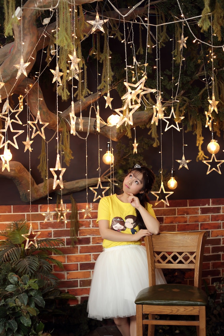 Photo of Ovilia Zhang wearing a tulle skirt, looking thoughtful, under a canopy of lights.