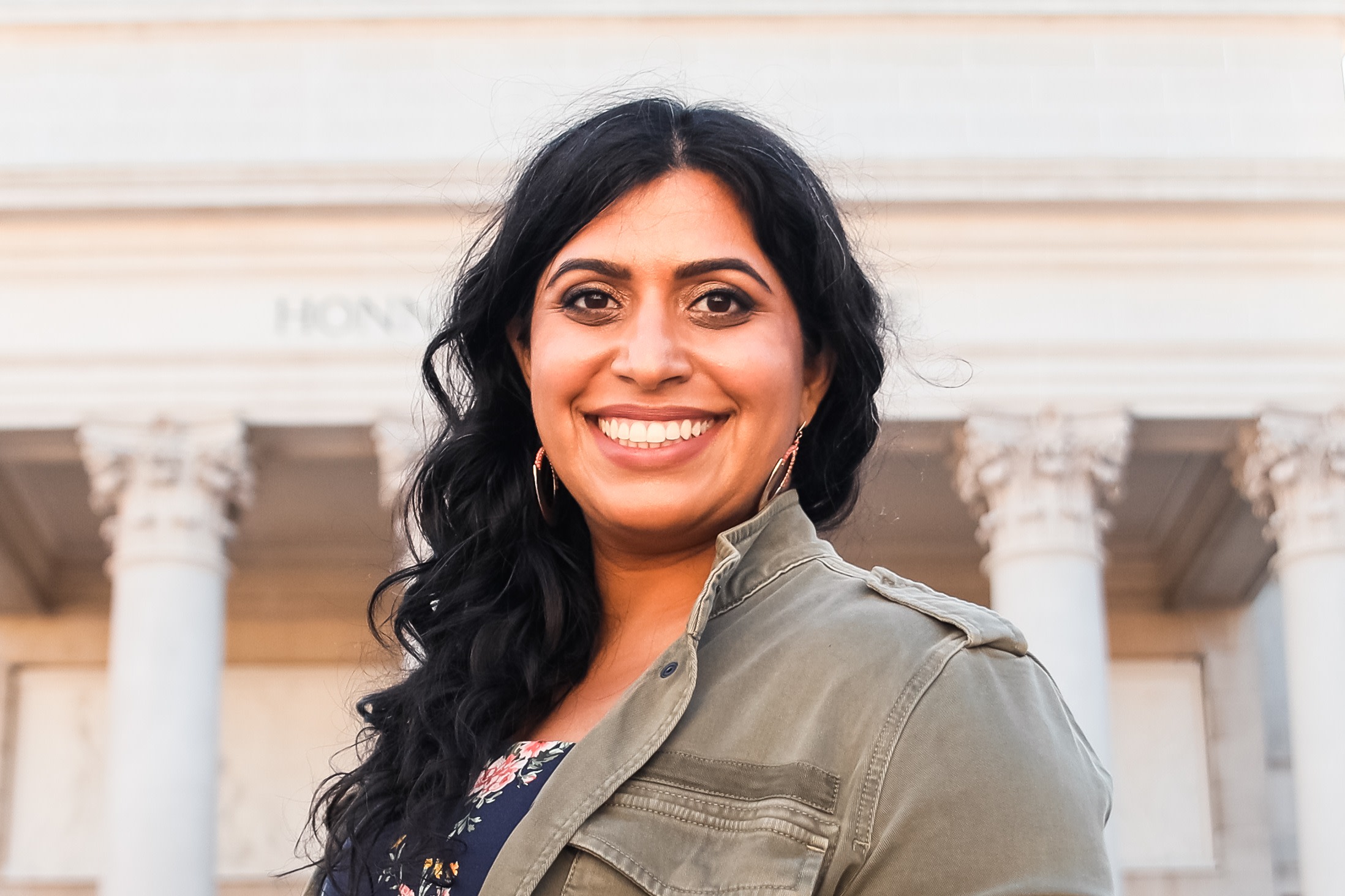 Author Neha smiling in front of a statuesque, column-lined building