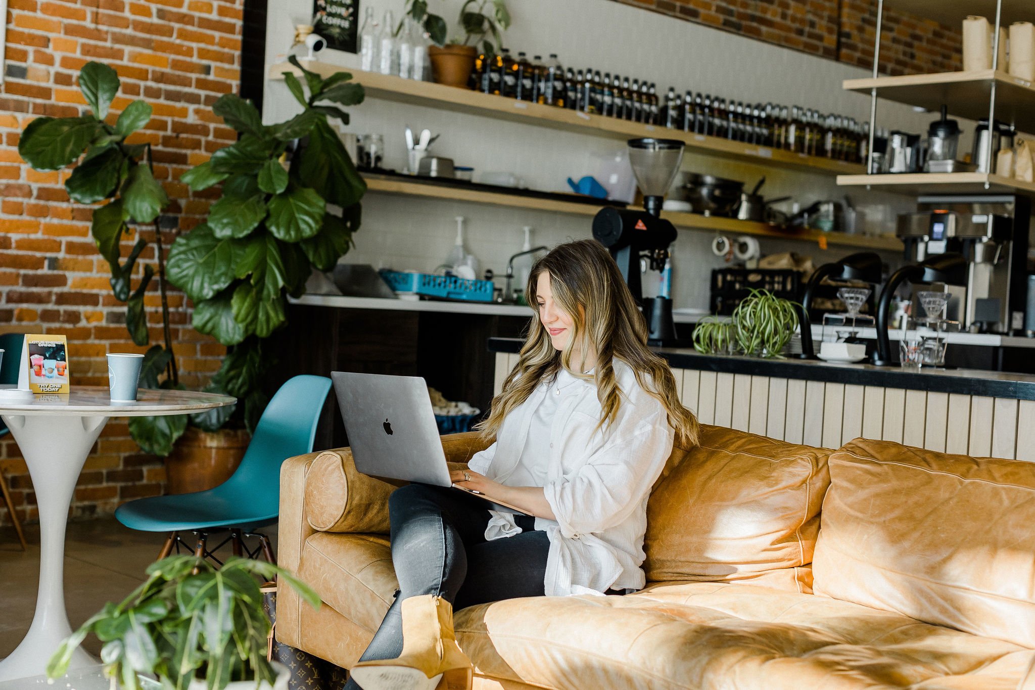 Author Rose sitting on a leather couch in a coffee shop, working on her laptop