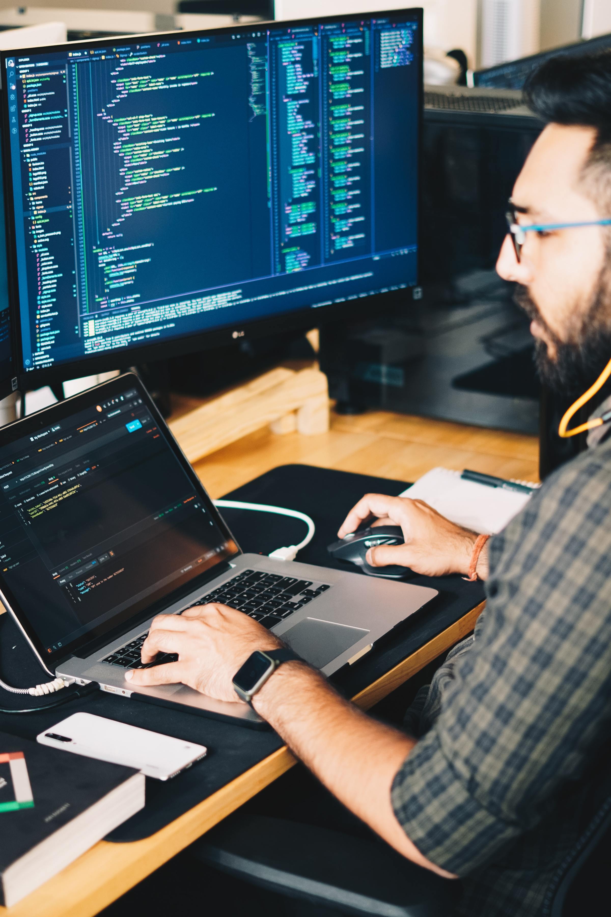 A person working on code on both their laptop and desktop