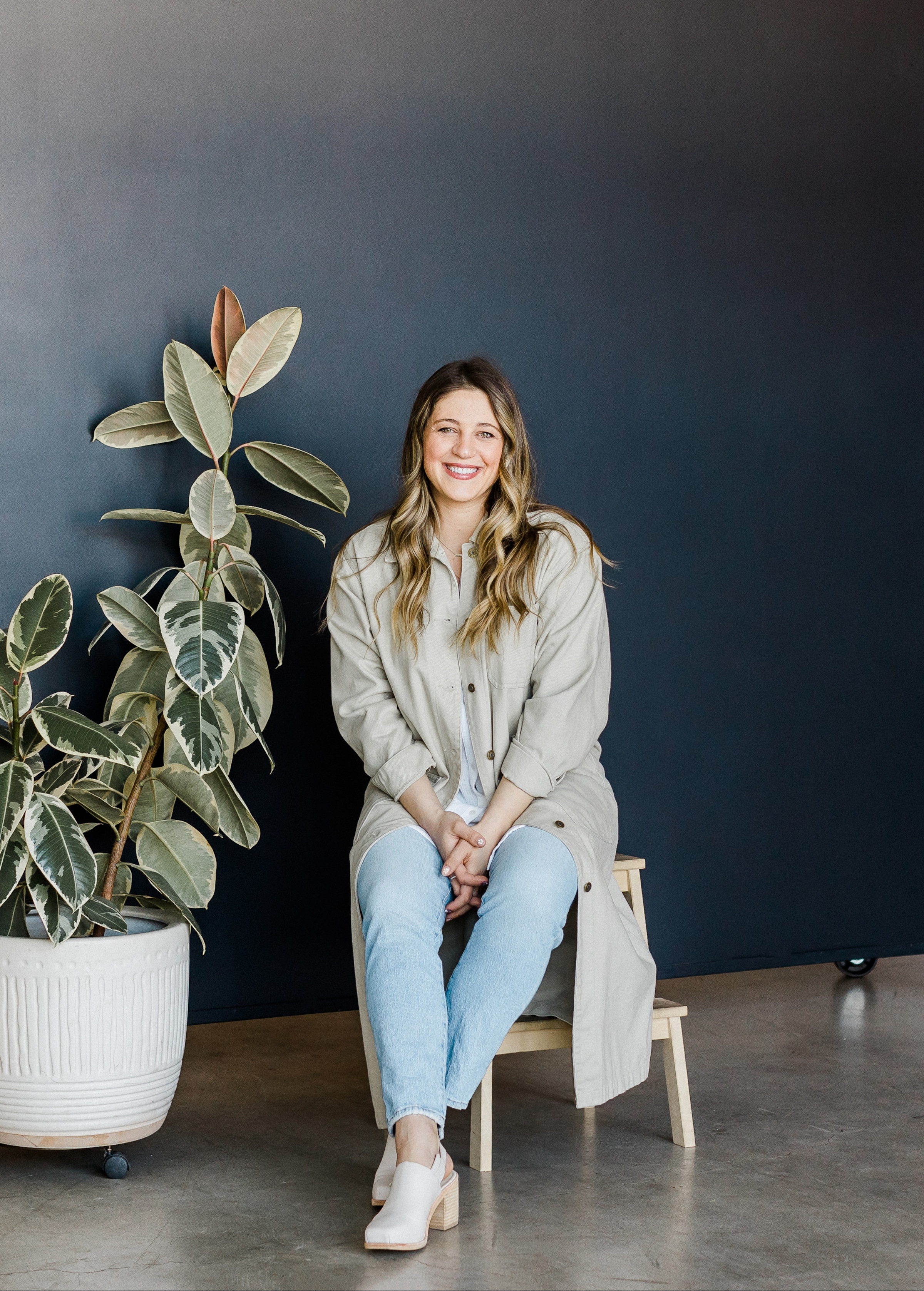 Author Rose smiling and sitting inside next to a large plant