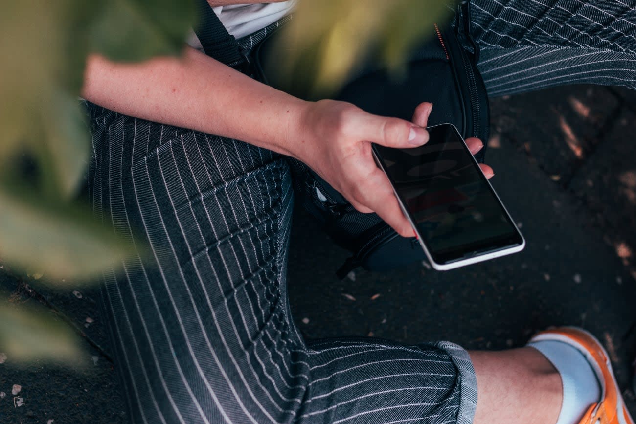 Photo of a person sitting outdoors on the ground and using a phone.