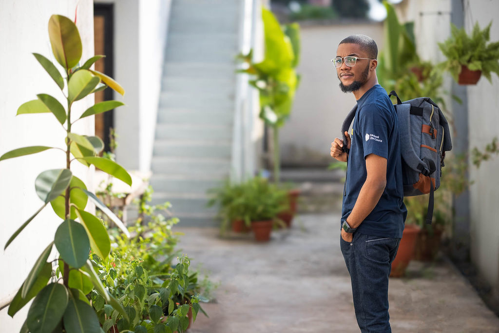 Author Adewale in a plant-lined walkway with his backpack