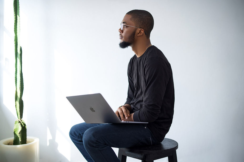 Author Adewale sitting next to a cactus with his laptop