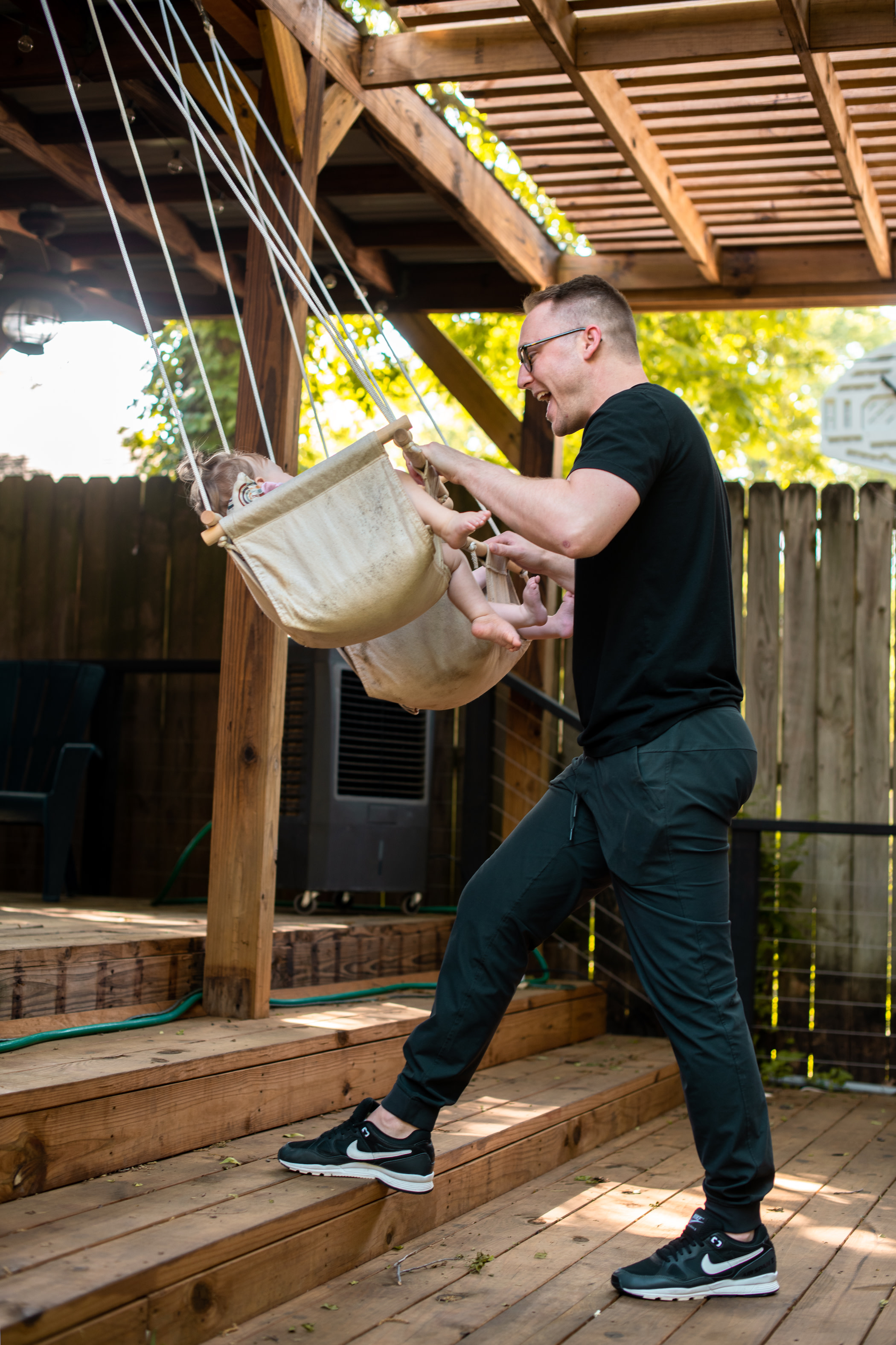 Author Aaron smiling as he pushes his twin children in swings on his back porch