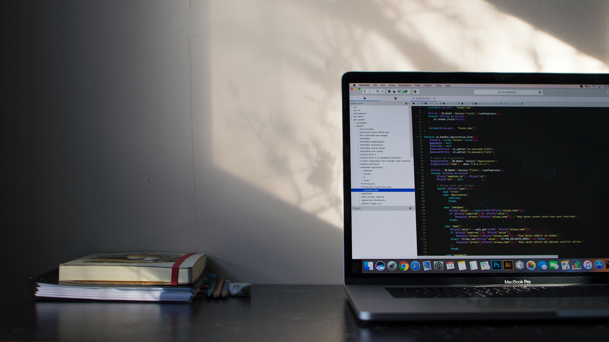 A laptop with code on the screen, sitting next to notebooks and pencils