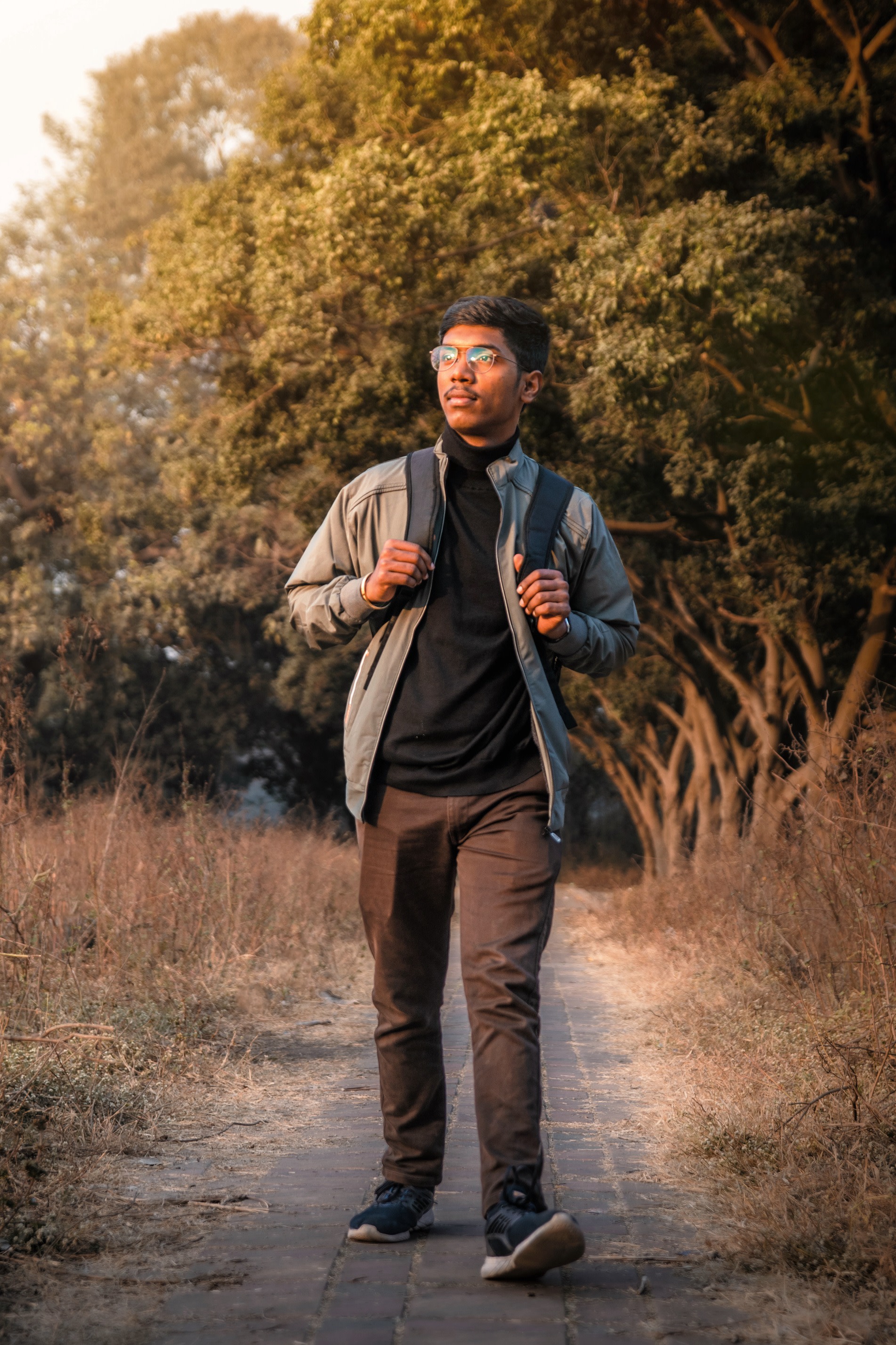 Author Rohan wearing a backpack and walking down a nature path in the middle of a field with trees behind him