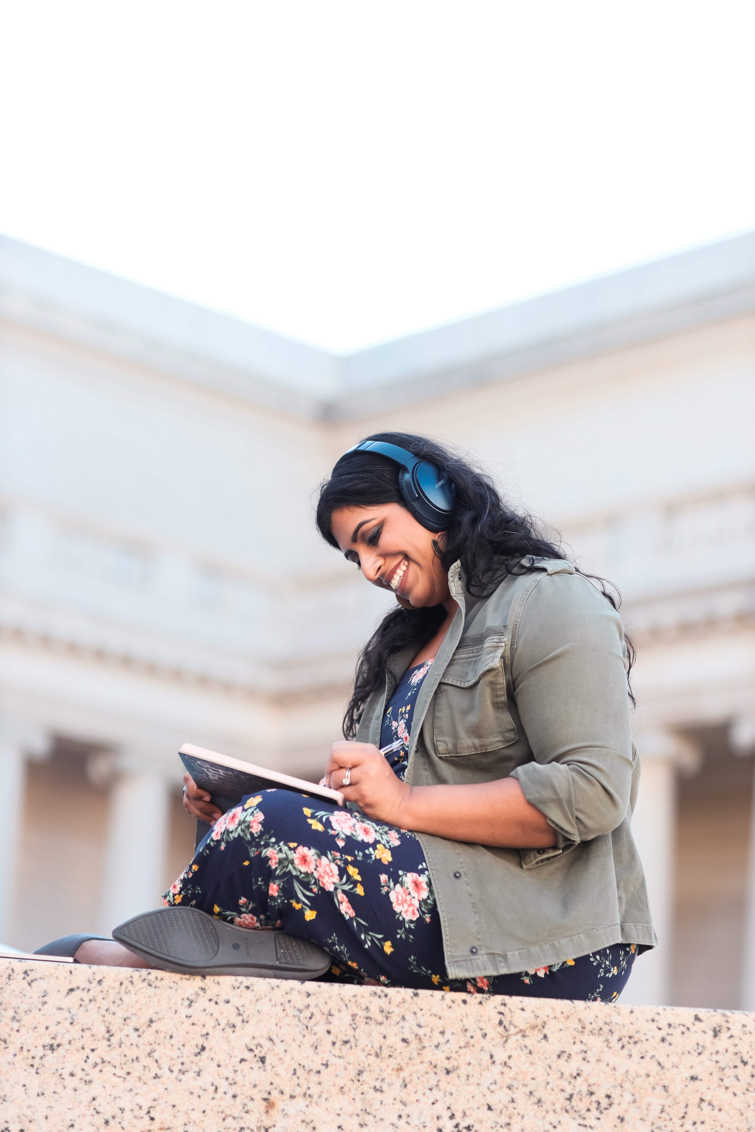 Author Neha sitting outside with her headphones on, smiling, and working on her tablet