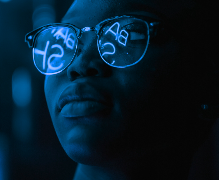 Woman's face with neon text reflecting off her glasses.