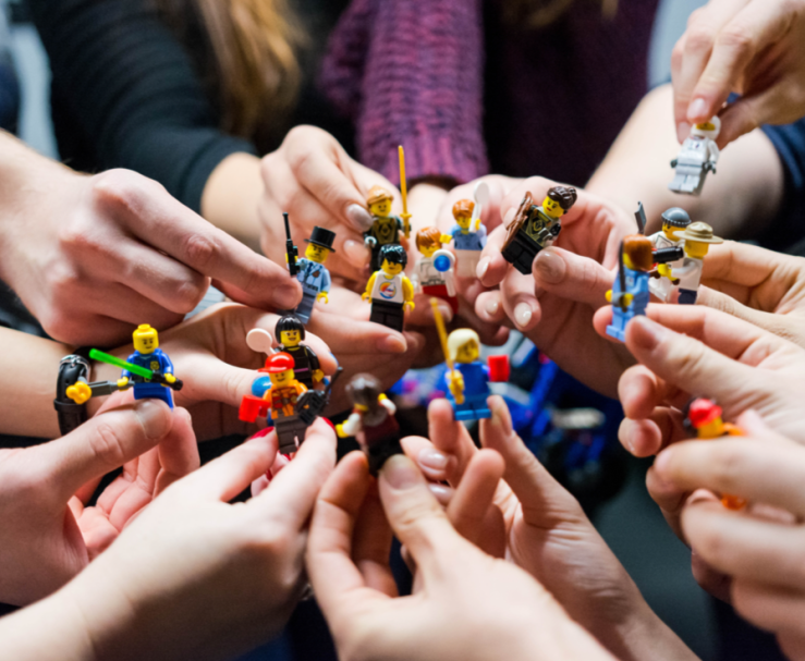 At least ten hands holding a variety of LEGO people.