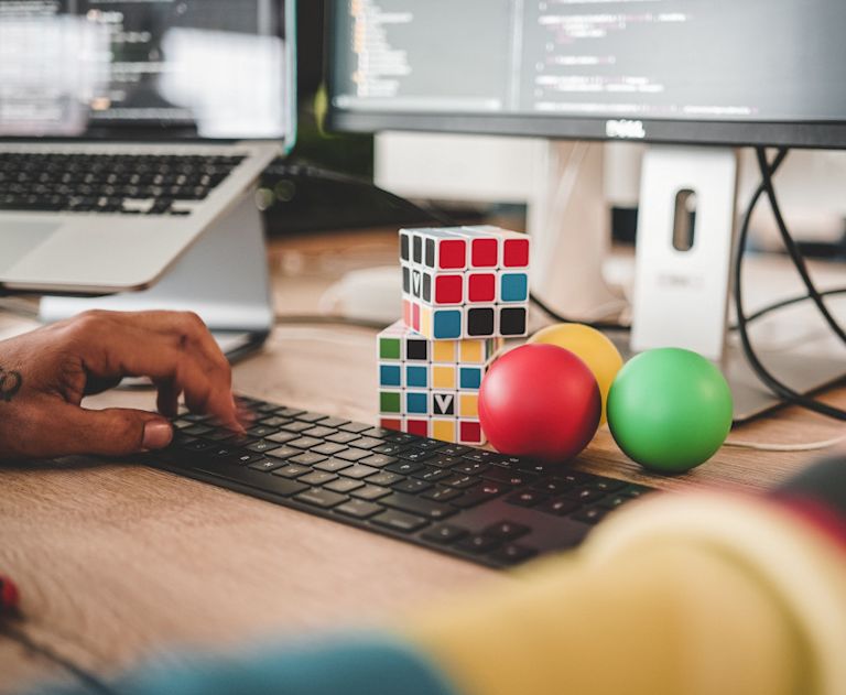 Person working at desk with laptop and second screen, plus puzzle cubes and juggling balls.