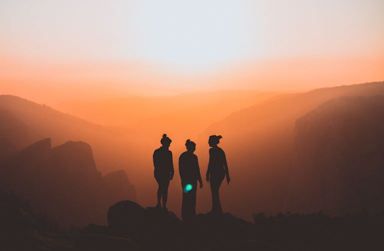 Three women watch the sun rise in a warm orange glow by  Karl Magnuson