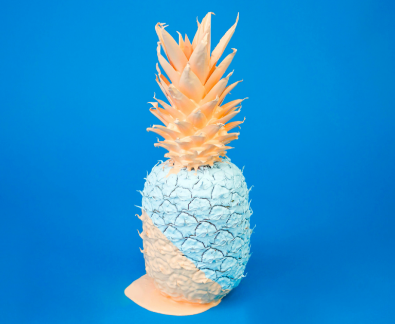 Pineapple painted pale orange and green sits on a blue background.