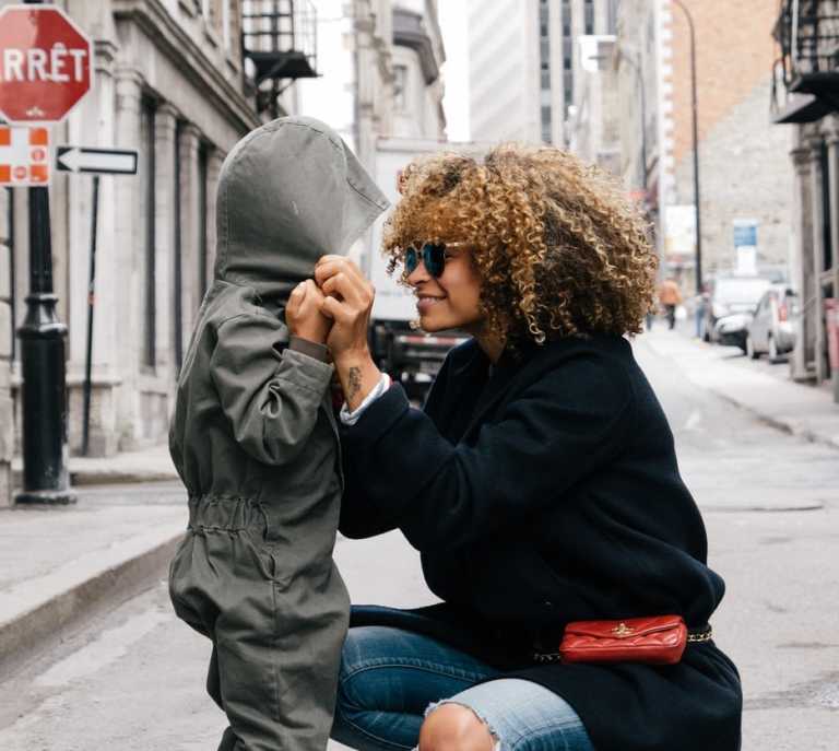 Mother adjusting her child's jumper in the street and smiling 