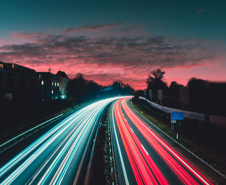 Time-lapse photo of highway road at dusk, a stream of white light on the left and red on the right.