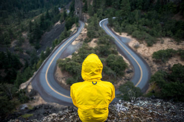 Person in yellow raincoat looking at road that goes in two different directions.