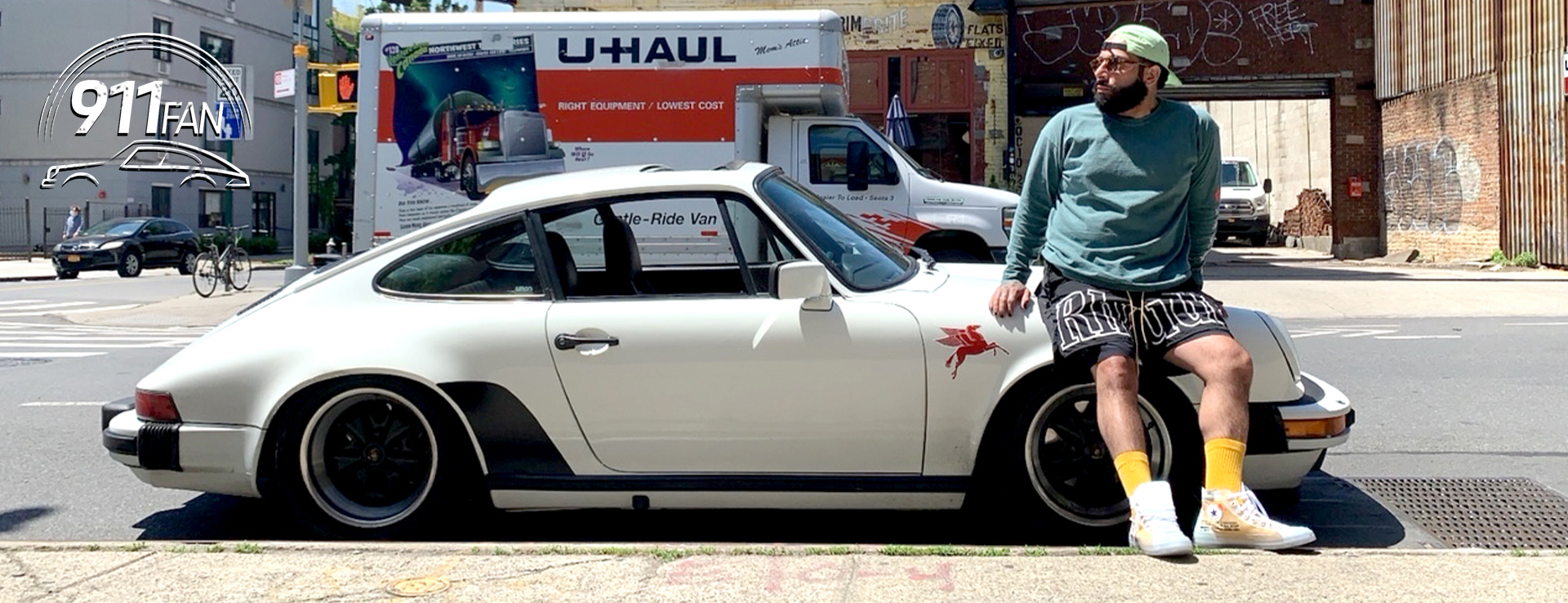Man wearing glasses sitting on bonnet of classic Porsche 911