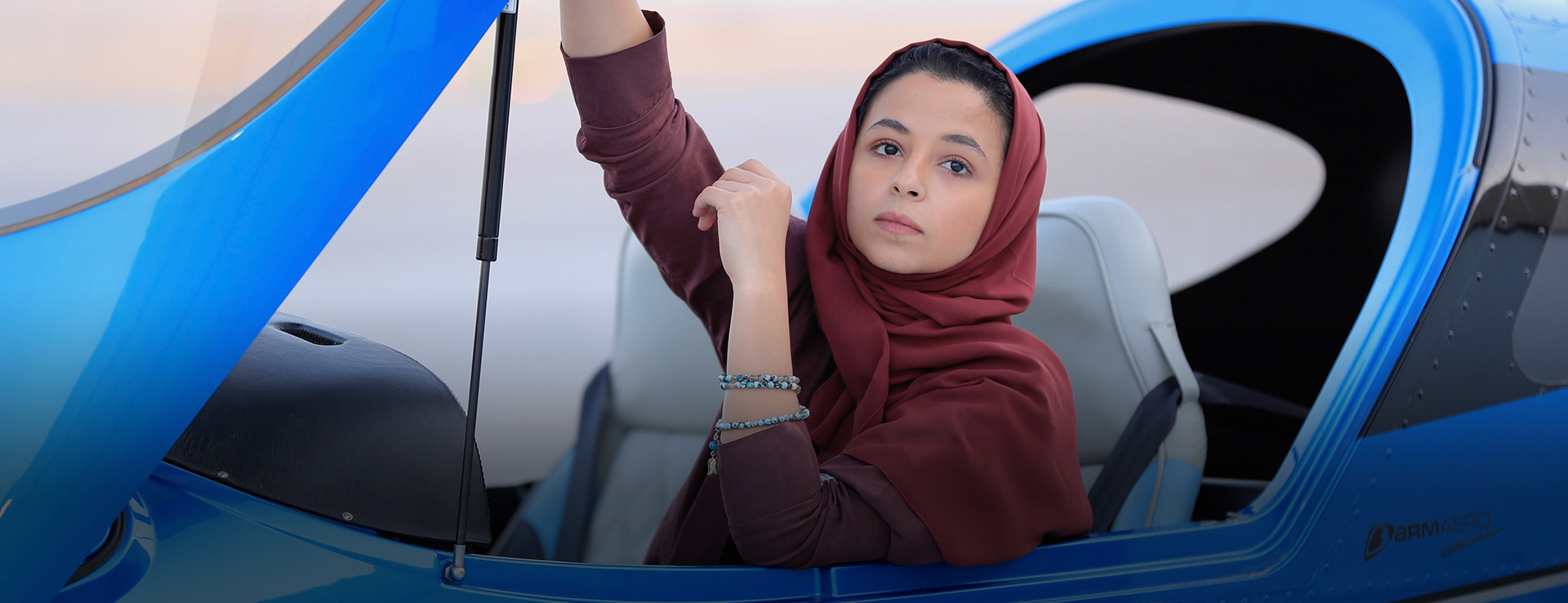 Woman in hijab sat in light aircraft, lifting its canopy