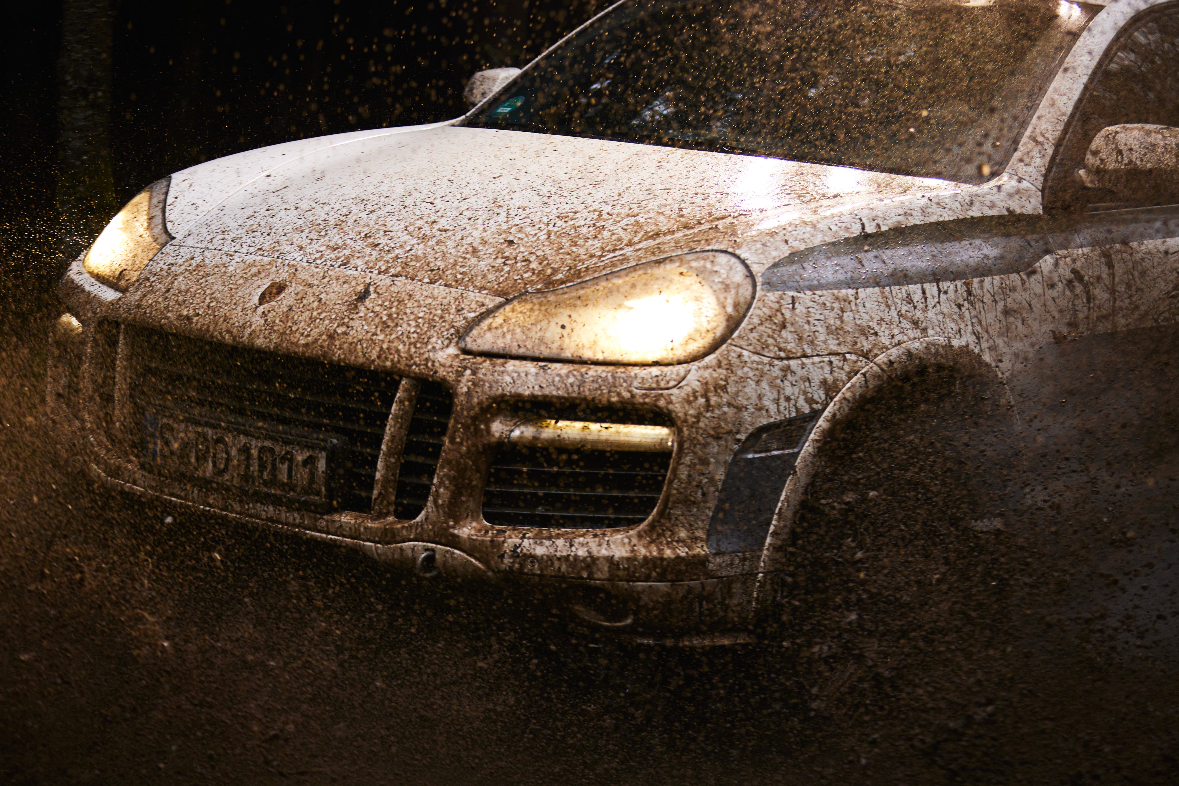 Mud-splattered, white, first-generation Cayenne with headlights on
