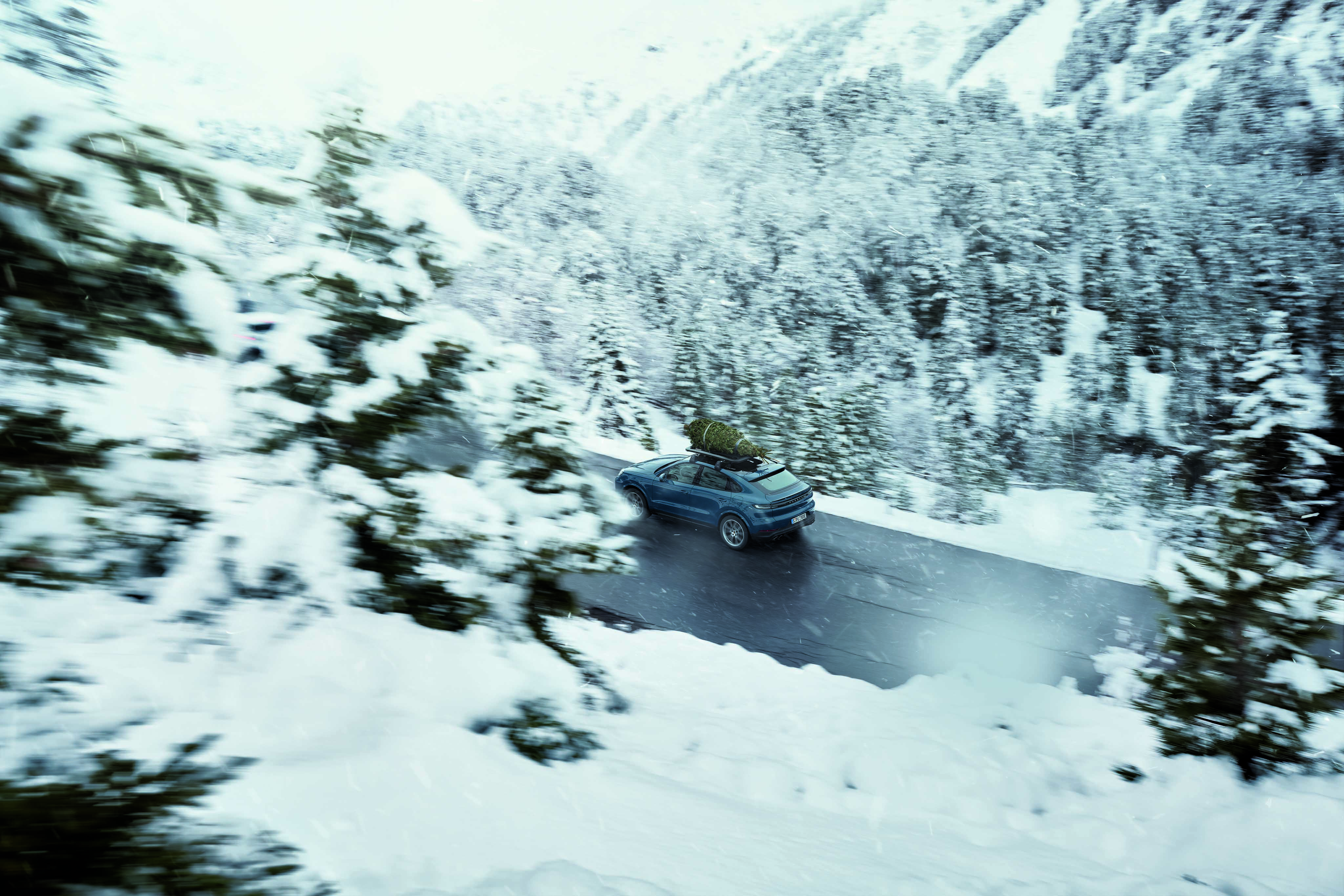 Blue Porsche Cayenne E-Hybrid Coupé with roof cage on snowy road
