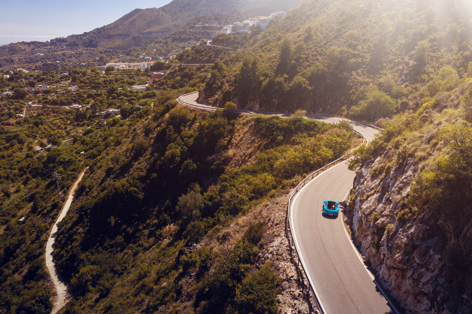 Winding, sunlit mountain road with blue Porsche 911