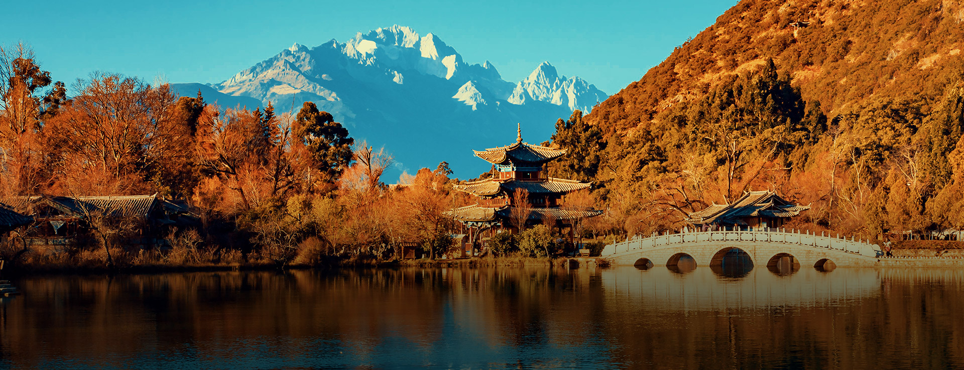 Chinese temple by a lake, mountain massif in the background