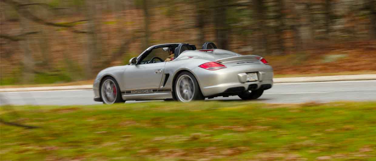 A Porsche Boxster Spyder driving on a tree-lined road