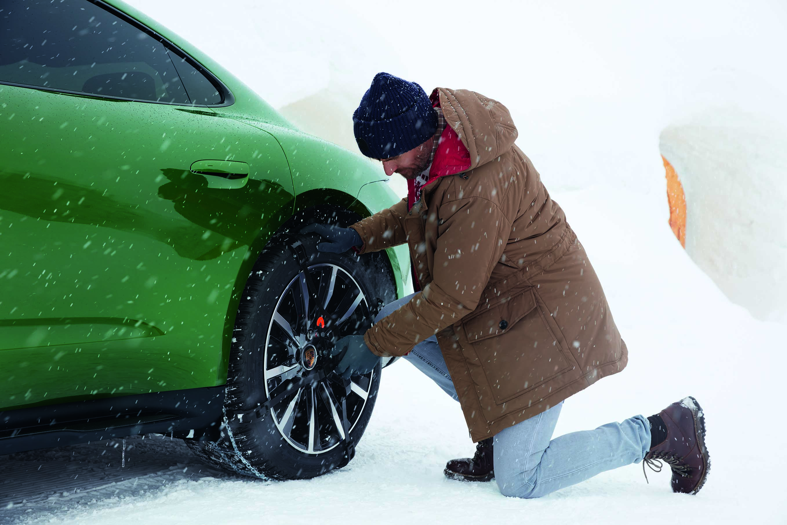 Man fits snow chains to tyres of green Porsche Taycan