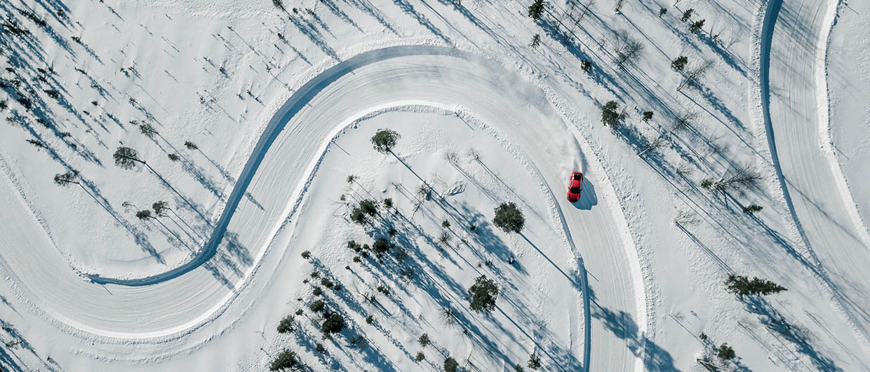 A bird's-eye view of a groomed racetrack in the snow. A red vehicle is drifting on it