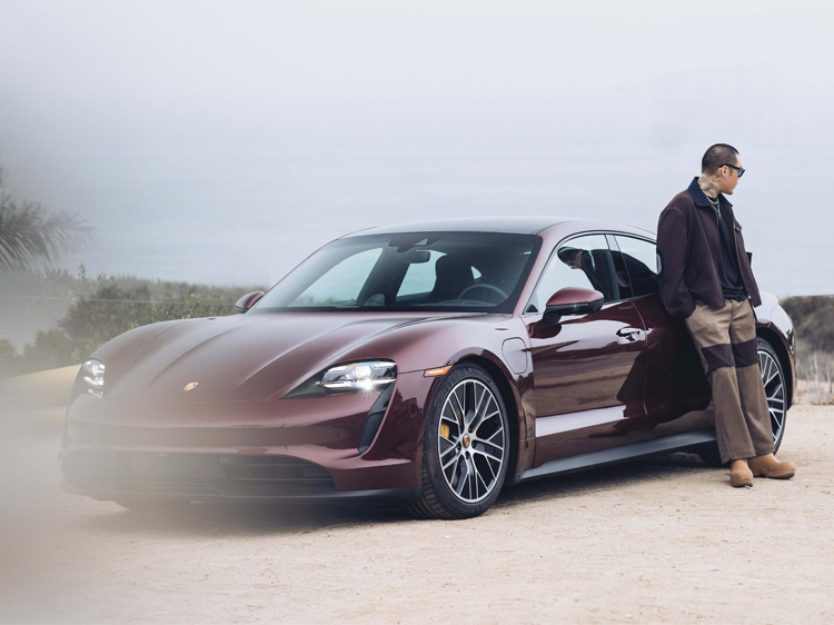 Man leans on electric Porsche Taycan parked on sandy ground