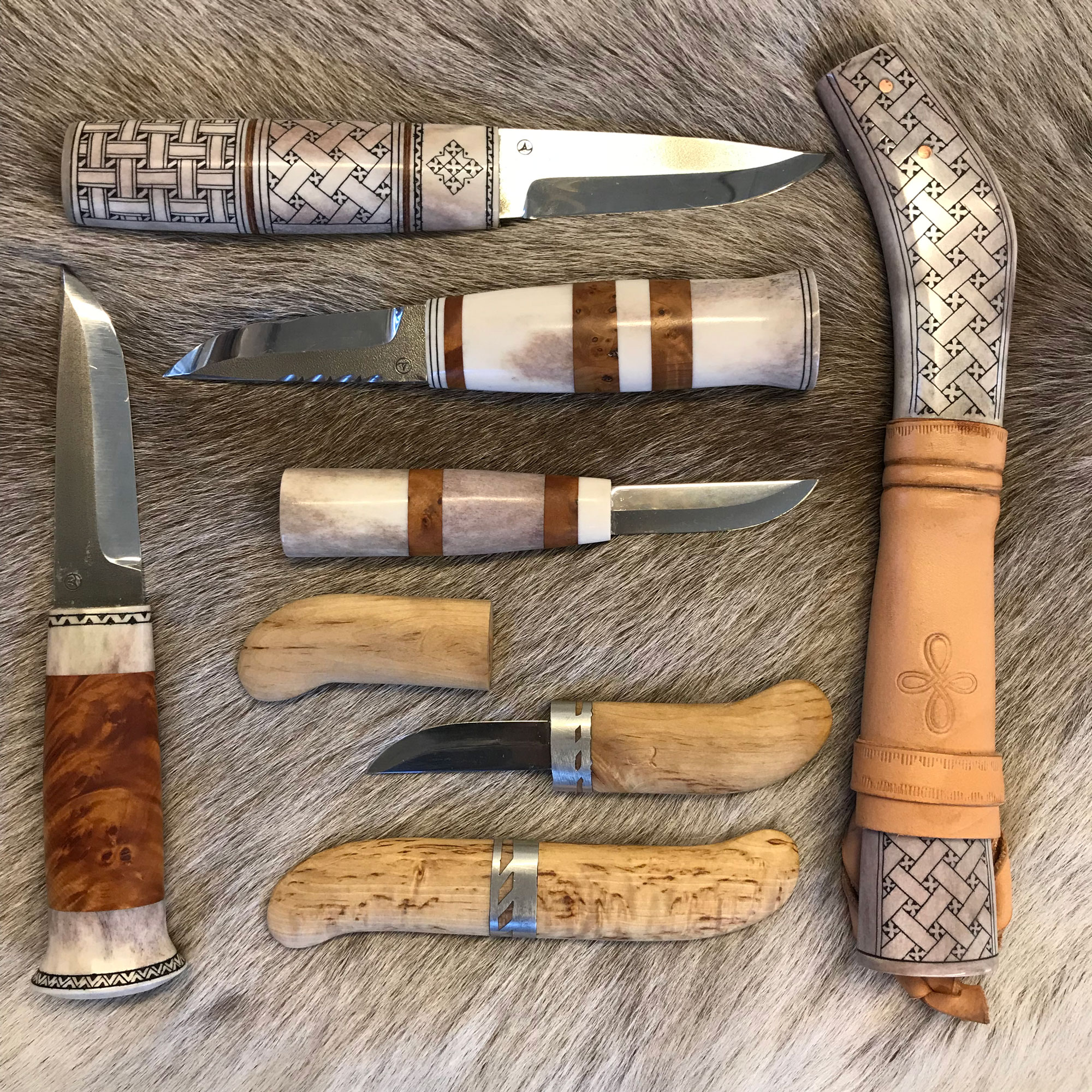 Various traditional puukko knives laid out on reindeer fur