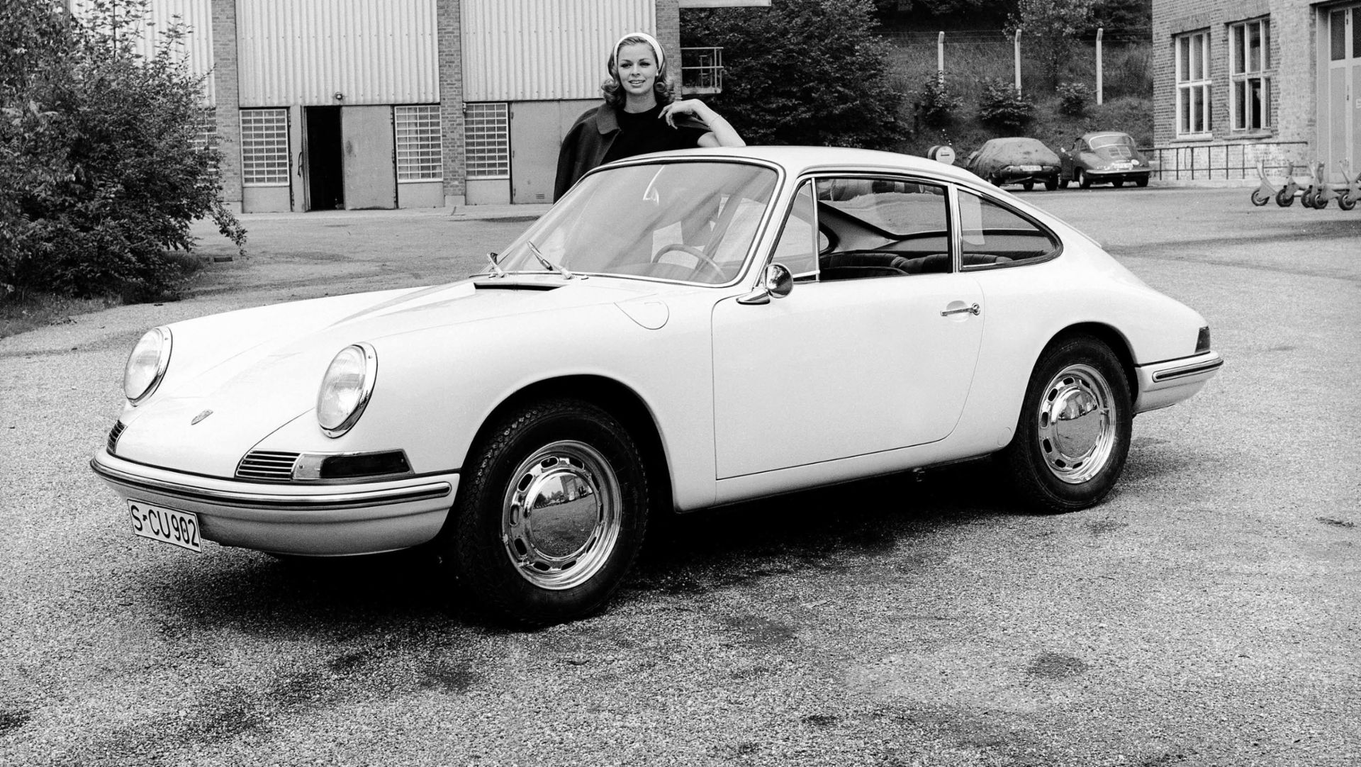 Black and white image of woman standing behind first Porsche 911