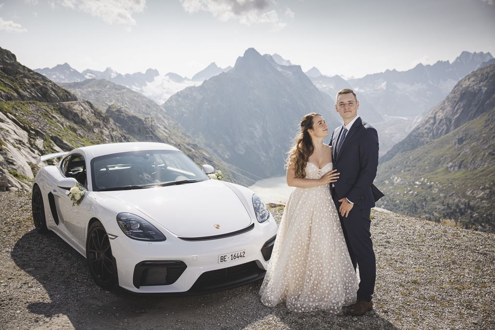 Bride and groom with Porsche 718 Cayman GT4, mountains behind