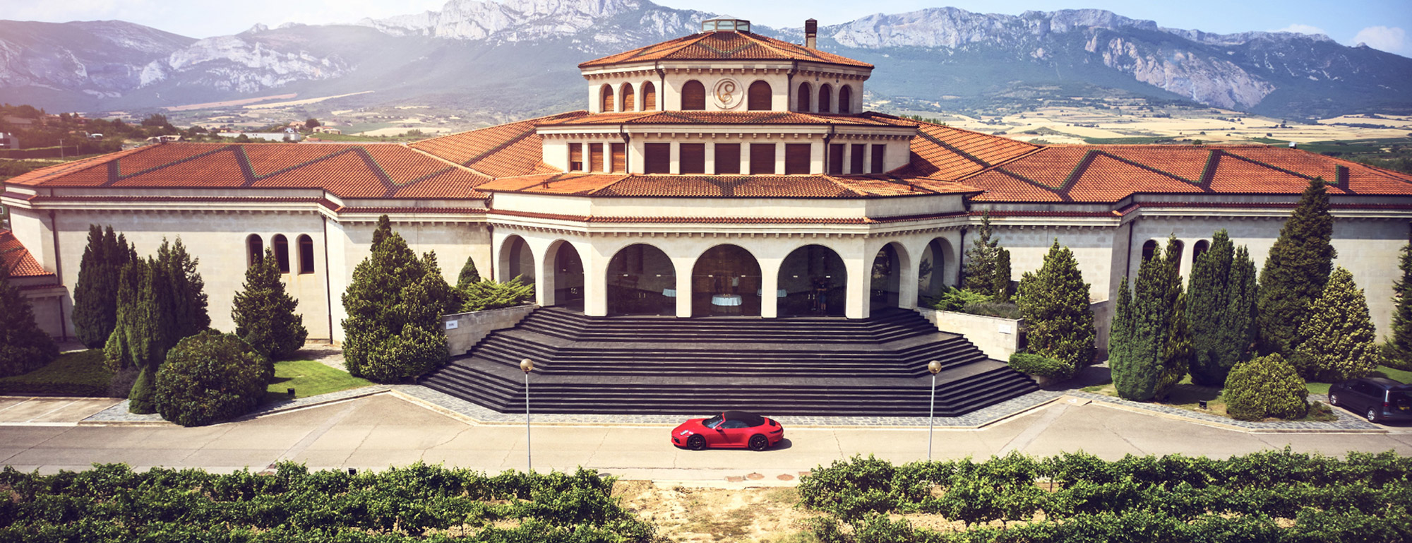 Porsche in front of large wine estate, mountain range behind