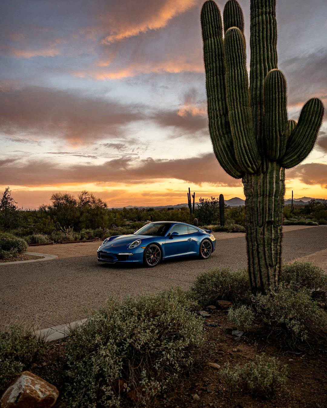 Blue Porsche 911 against desert sunset with saguaro cactus